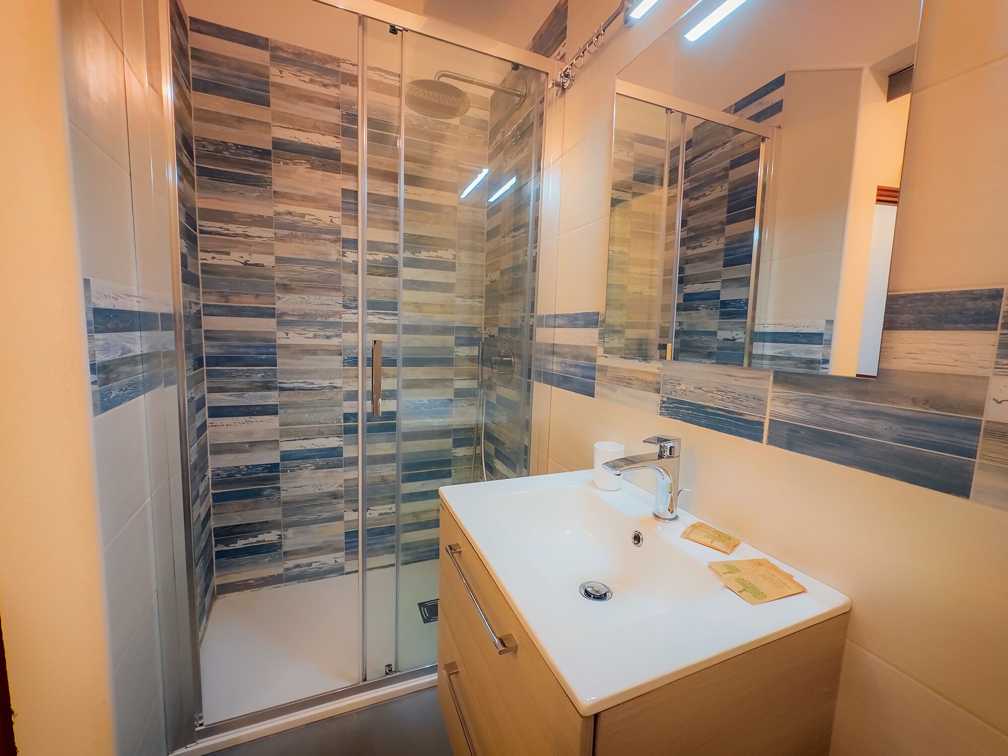 A modern bathroom with a glass shower enclosure, a white sink, and a large mirror.