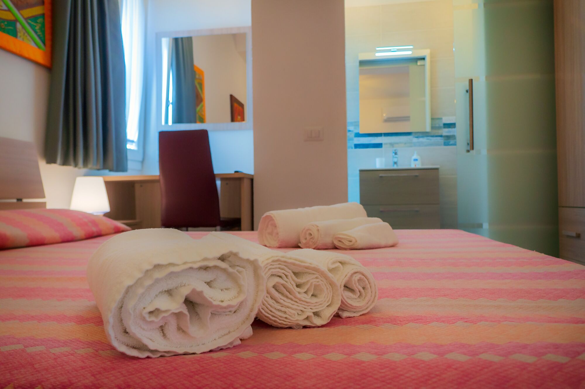 Une chambre d’hôtel avec un lit, un bureau, une chaise et une salle de bain visible à travers une porte ouverte.