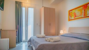 Quarto de hotel com cama, guarda-roupa, escrivaninha e janela com cortinas.