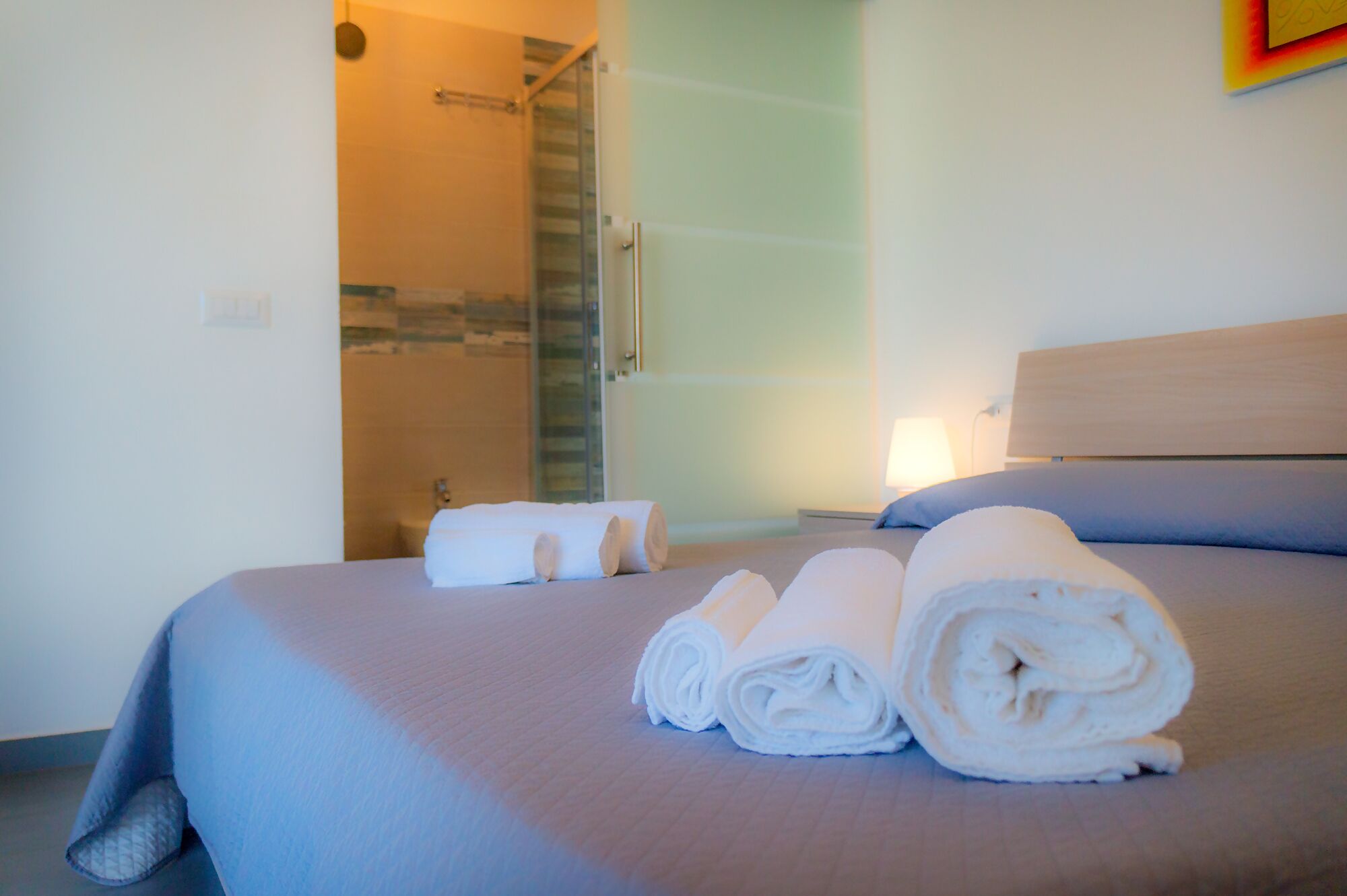 A hotel room with a bed, a bathroom with a shower, and a towel on the bed.