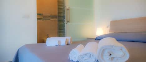 A hotel room with a bed, a bathroom with a shower, and a towel on the bed.