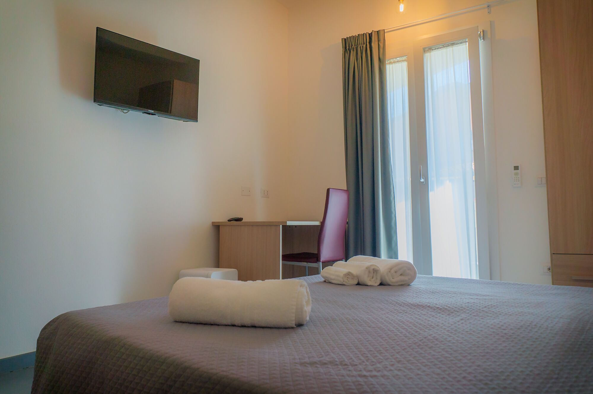 Habitació d'hotel amb un llit, escriptori, cadira, televisió i finestra amb cortines.