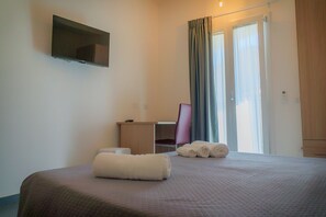 Habitación de hotel con cama, escritorio, silla, televisor y ventana con cortinas.