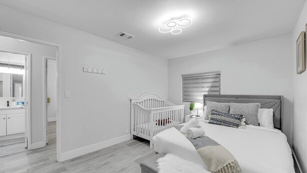 A modern bedroom with a white crib, a large bed with grey bedding, and a bathroom visible through an open door. - The Sweet Home｜Central Located｜Perfect for Family (Las Vegas)
