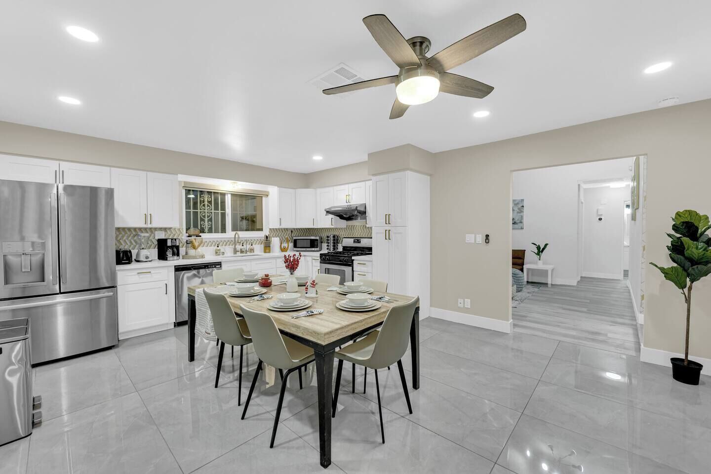 Une cuisine moderne avec des meubles blancs, une table à manger pour quatre personnes et un ventilateur de plafond.