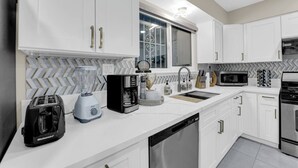 A modern kitchen with white cabinets, a herringbone tile backsplash, a built-in dishwasher, a toaster, a coffee maker, and a microwave. - The Sweet Home｜Central Located｜Perfect for Family (Las Vegas)