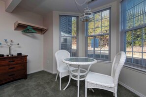 A room with a round glass table, two white wicker chairs, a wooden dresser, and a hanging light fixture. - Lakeview Condo (Kimberling City)