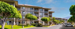 A multi-story residential building with balconies, a parking lot, and a clear sky. - 2-bedroom condo in tranquil Maui perfect for relaxing getaways (Maui)