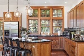 Une cuisine moderne avec des meubles en bois, un grand îlot central, des appareils électroménagers en acier inoxydable et de grandes fenêtres.