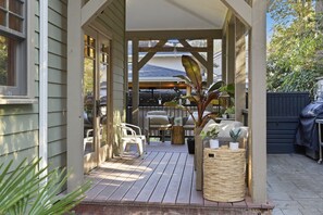 Un patio extérieur abrité, doté d’une terrasse en bois, de mobilier d’extérieur et de plantes en pot.