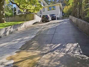 Ein gepflasterter Weg führt zu einem Haus mit Garage, umgeben von Bäumen und einer Betonmauer.