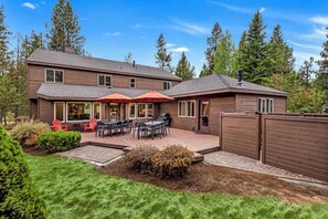 Una casa de dos pisos con un patio, mobiliario exterior y un patio trasero cercado.