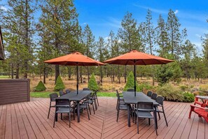 An outdoor deck with a table and chairs, two umbrellas, and a wooden deck. - On Golf Course, Walk to Park, Hot tub, SHARC (Sunriver)