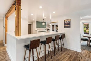 Una cocina moderna con una isla blanca, taburetes de bar y vistas al exterior.
