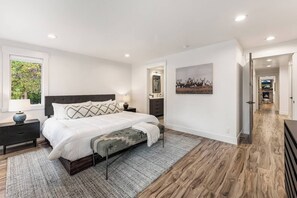 Un dormitorio moderno con una cama grande, una mesita de noche, una lámpara, una obra de arte en la pared y vistas al pasillo.