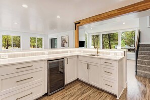 A modern kitchen with white cabinetry, a built-in dishwasher, and a large window offering a view of trees. - On Golf Course, Walk to Park, Hot tub, SHARC (Sunriver)