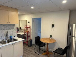 A compact kitchen with a sink, cabinets, a refrigerator, and a dining area with chairs and a table. - Chez Rose Charming Knowlton Retreat -Walk to Cafés and Shops (Lac-Brome)