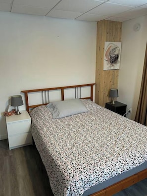 A single bed with a patterned bedspread, a wooden headboard, two bedside tables with lamps, and a wall-mounted artwork. - Chez Rose Charming Knowlton Retreat -Walk to Cafés and Shops (Lac-Brome)