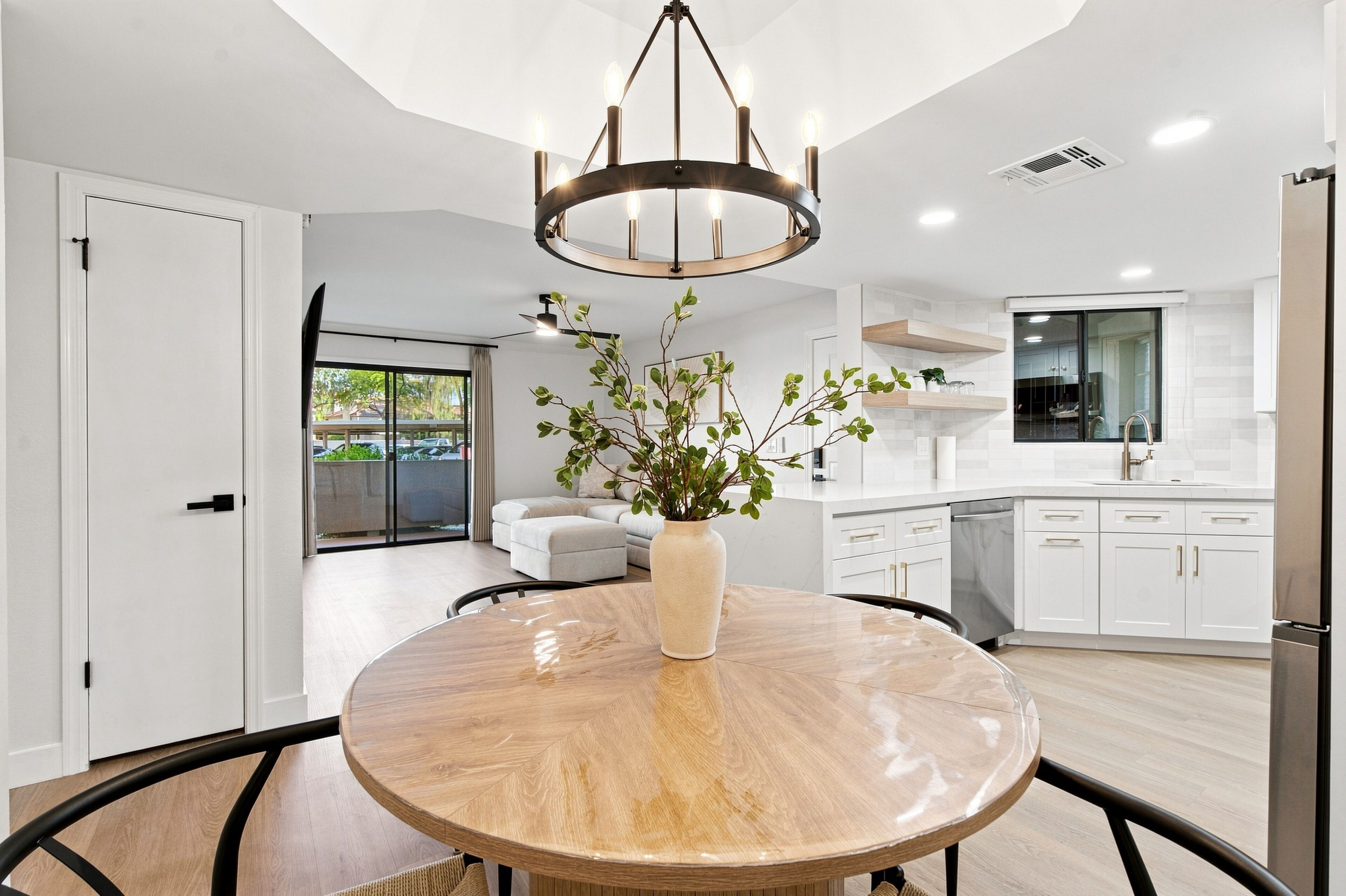 A modern kitchen with white cabinets, a stainless steel refrigerator, and a dining area with a round table and chairs.
