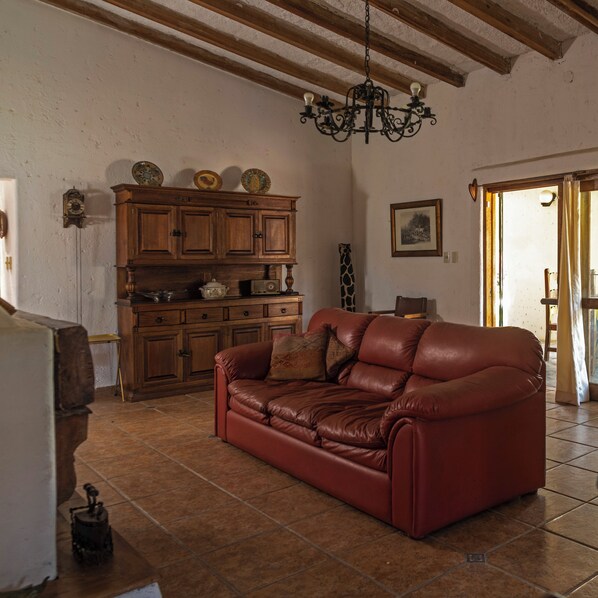 A living room with a leather sofa, wooden cabinets, a chandelier, and a tiled floor.