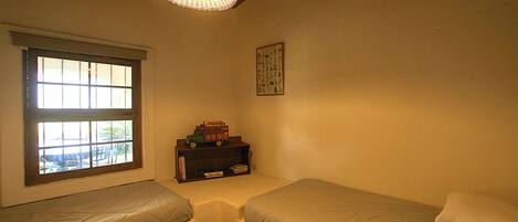 A room with two beds, a window, a hanging light fixture, and a small shelf with books and a toy car.