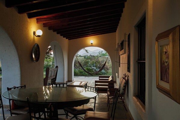 A covered patio with a table and chairs, a hammock, and a view of greenery and mountains. - Nature Retreat 4BR with Pool in Cañete (Quilmaná)