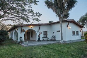 A white building with a tiled roof, multiple windows, and a porch with benches.