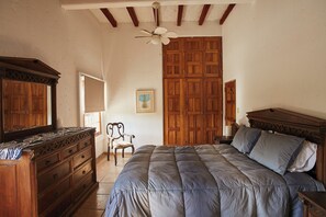 A bedroom with a large bed, wooden wardrobe, a chair, and a ceiling fan.