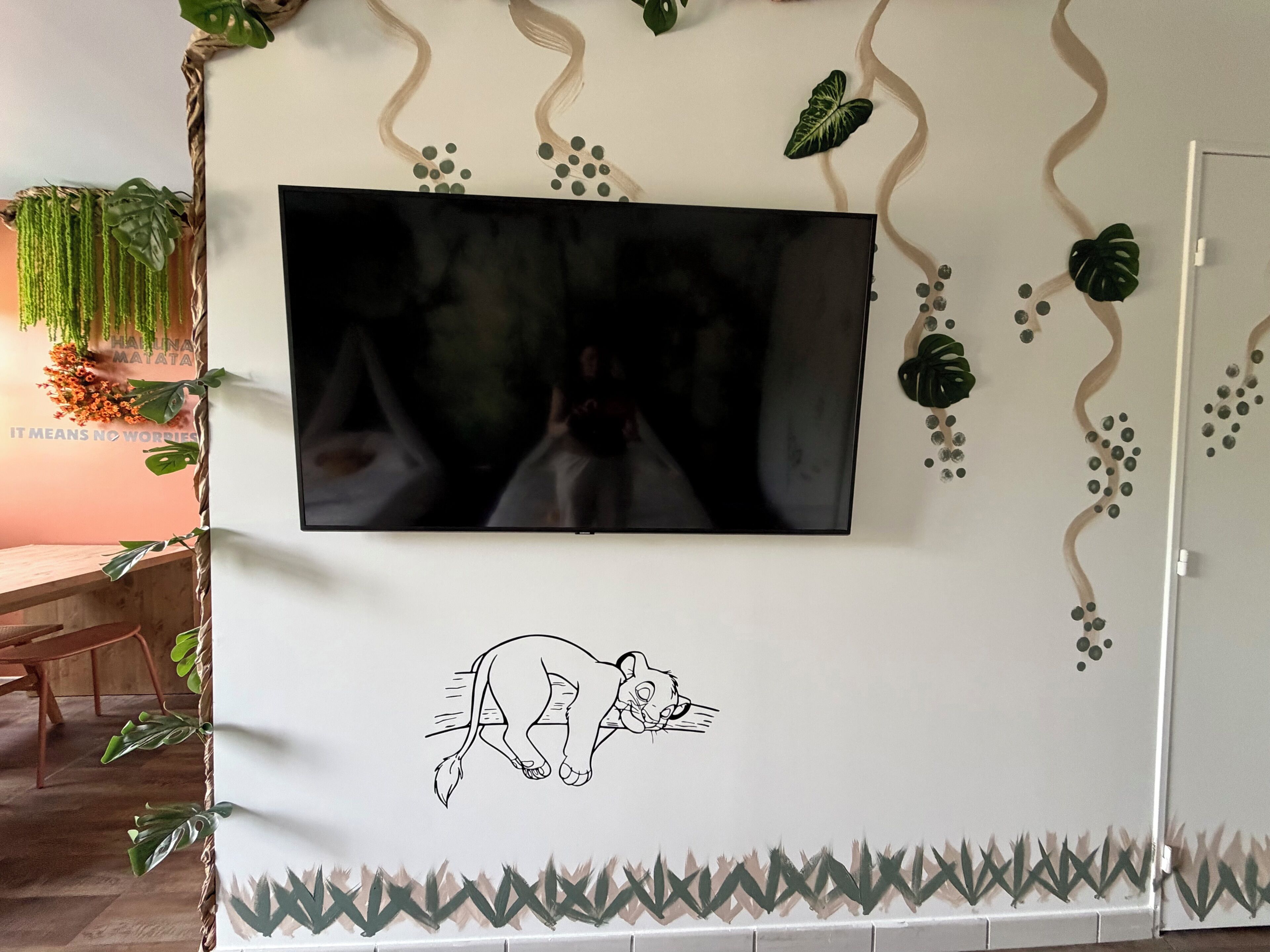 A wall-mounted television with a cartoon character, surrounded by wall art and greenery.