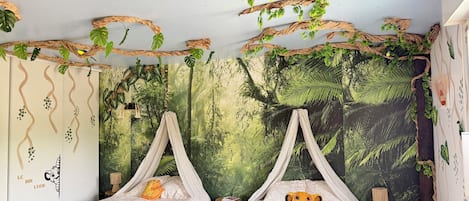 Een kamer met twee bedden, elk voorzien van een hemelbed, en een muurschildering van een bos op de wand.
