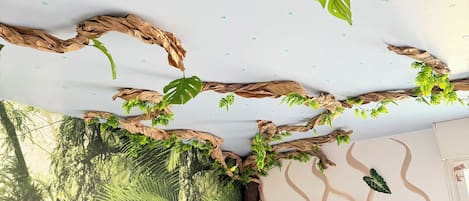 Una habitación con una pared decorada con un mural de motivos naturales, una planta colgante y un letrero que dice 'SIMBA LODGE'.