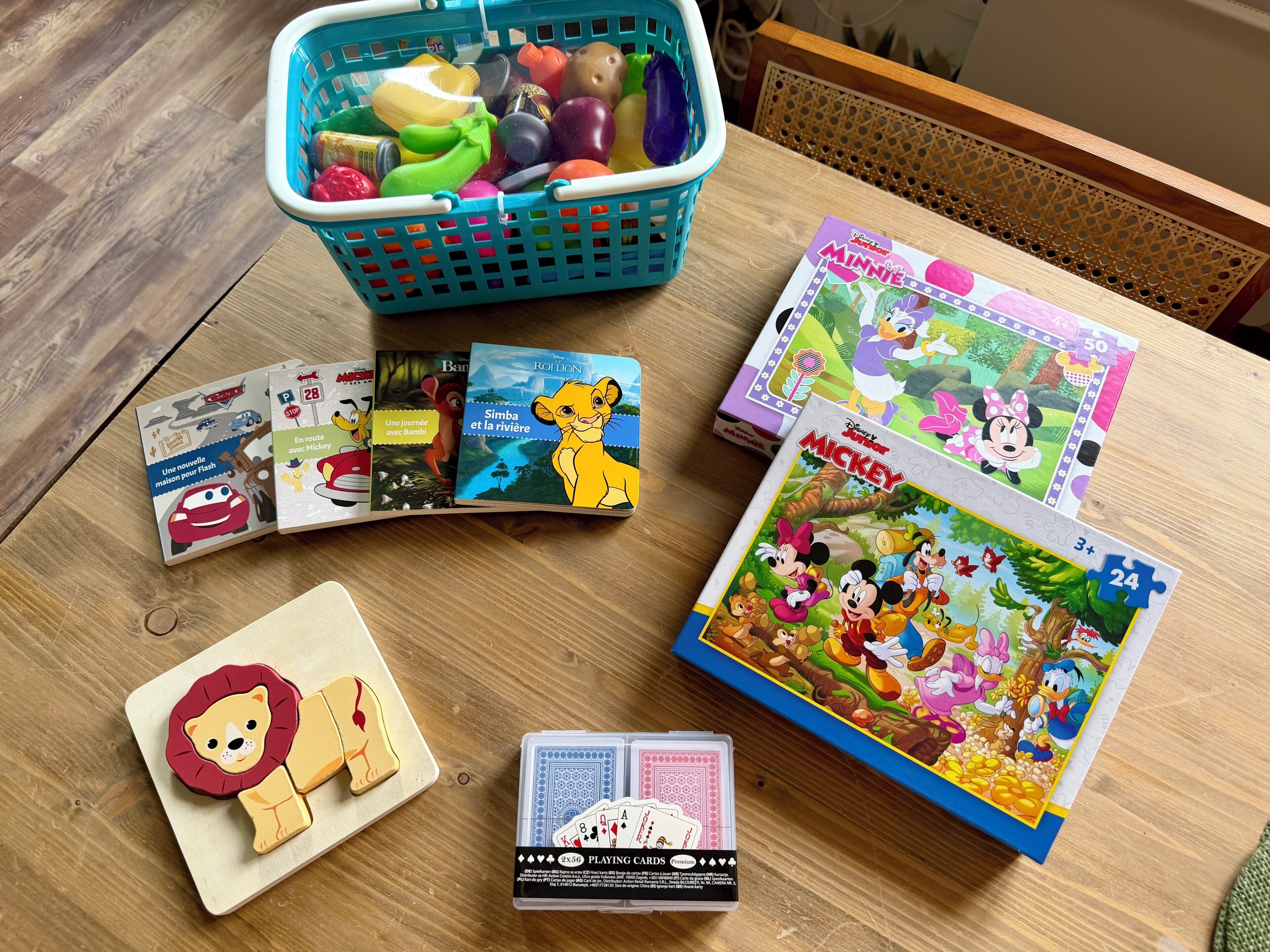 Une table avec des livres pour enfants, une voiture jouet, un puzzle et un panier rempli de jouets.