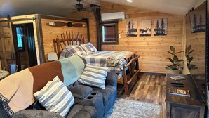 A cozy cabin-style room with a sofa, a wooden bed, a ceiling fan, and a wall-mounted air conditioner.