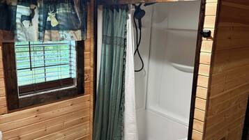 A bathroom with a wooden interior, a window with blinds, a shower, and a toilet.