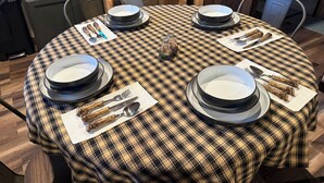 A round dining table with a plaid tablecloth, surrounded by chairs, and set with plates, bowls, cutlery, and napkins.