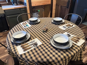 A round dining table with a plaid tablecloth, surrounded by chairs, and set with plates, bowls, cutlery, and napkins.
