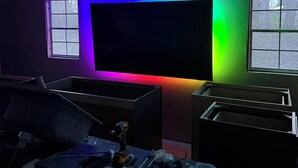 A room with a large flat-screen TV mounted on the wall, a window, and a workbench with tools.