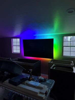 A room with a large flat-screen TV mounted on the wall, a window, and a workbench with tools.
