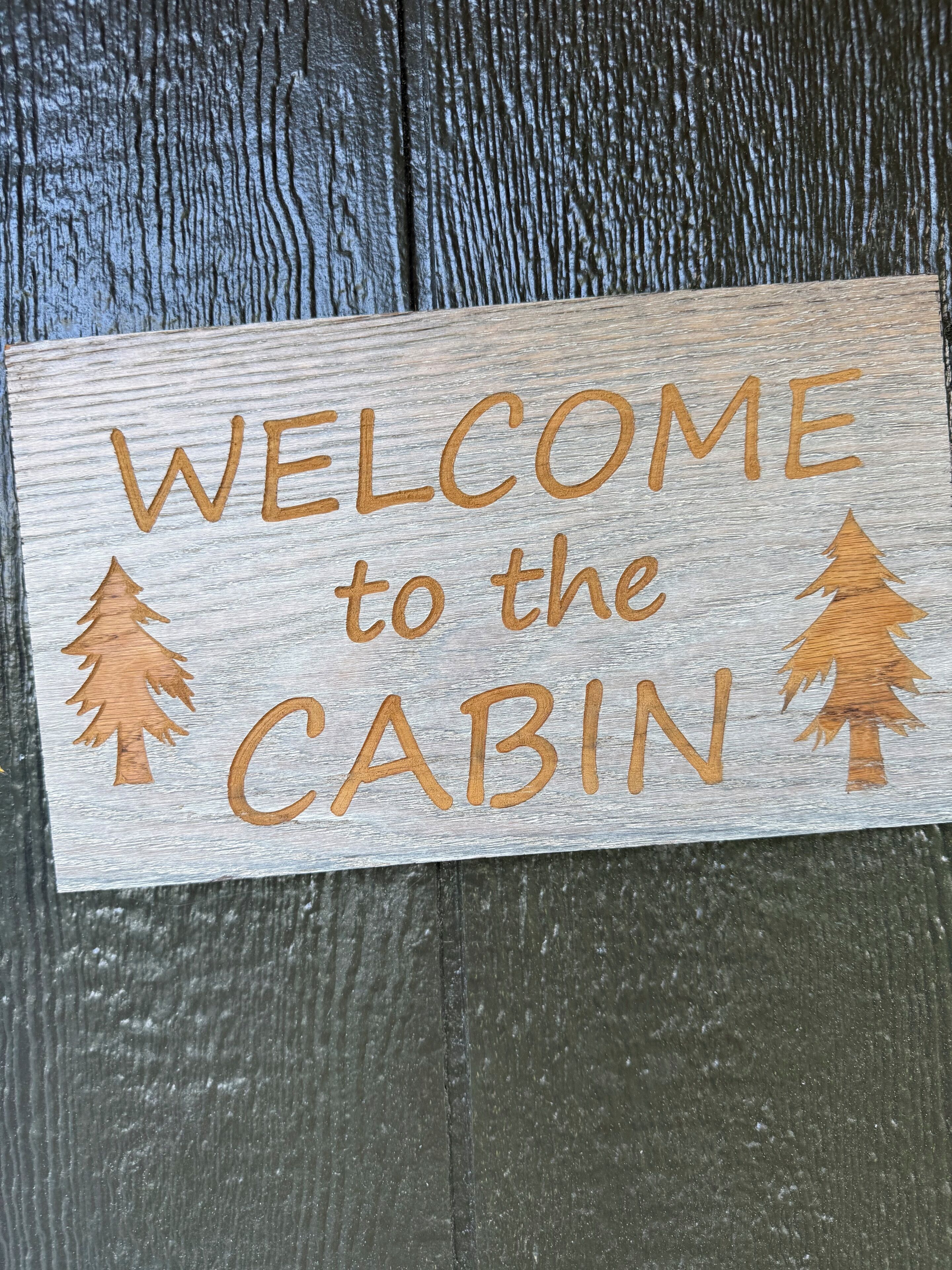 Une enseigne en bois portant l’inscription « BIENVENUE AU CHALET » et représentant deux silhouettes d’arbres.