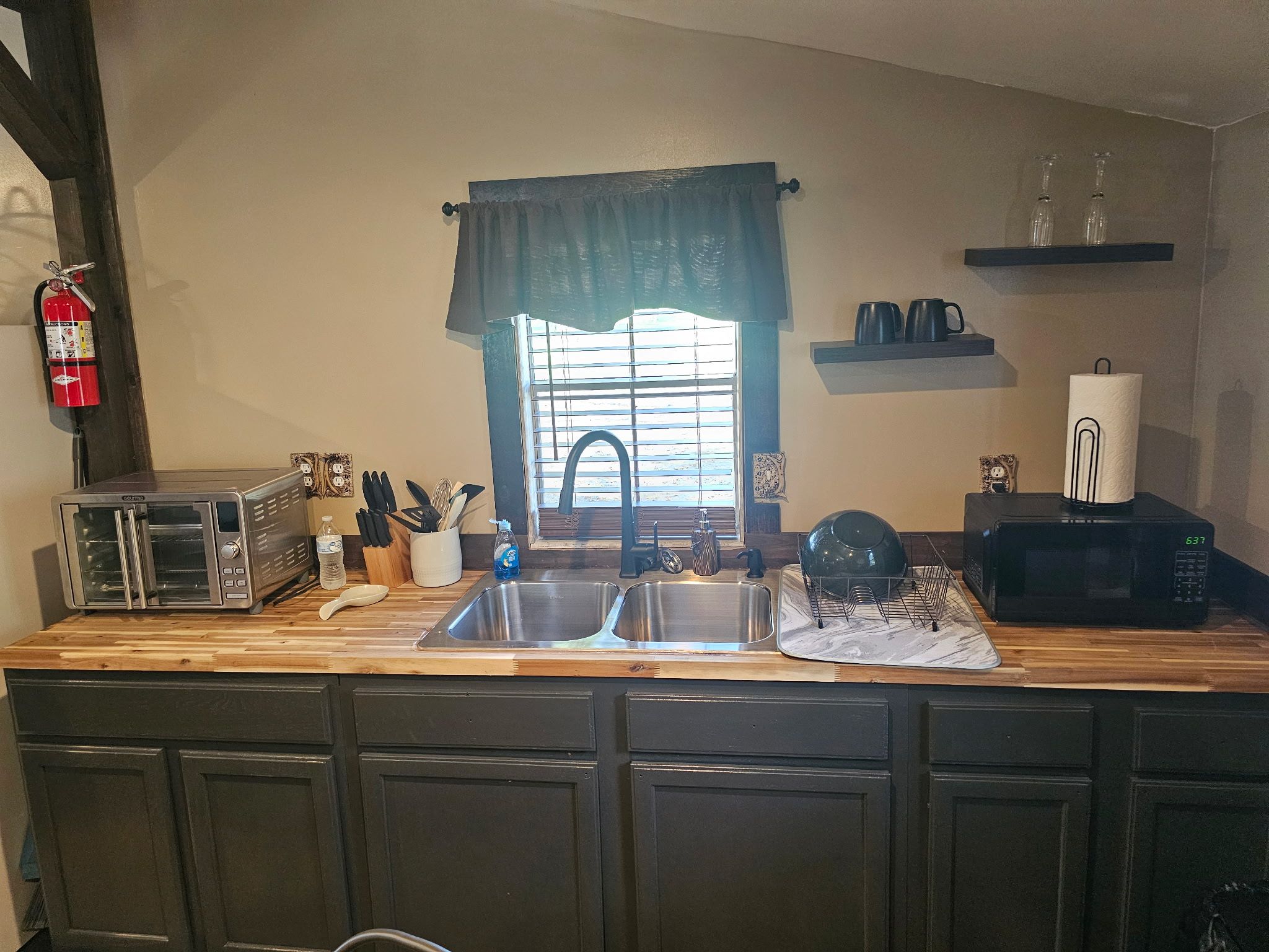 A kitchen with a double sink, a toaster, a microwave, and a fire extinguisher.