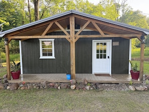 A small cabin with a wooden porch, two windows, and a door.