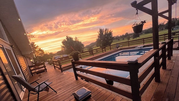 A wooden deck with a pool, outdoor furniture, and a view of the sunset.