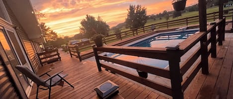 A wooden deck with a pool, outdoor furniture, and a view of the sunset.