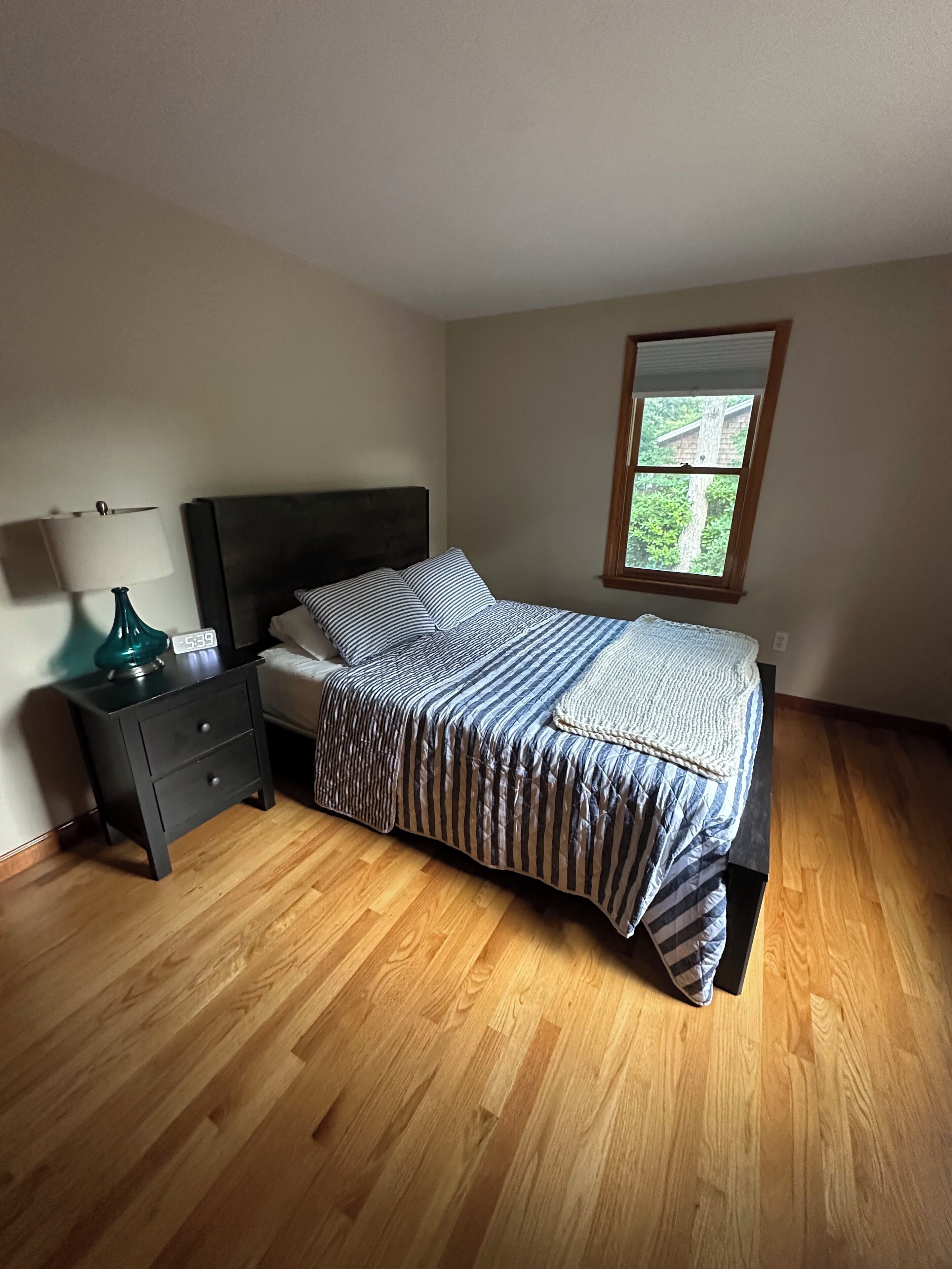 A bedroom with a bed, a nightstand, a lamp, and a window.