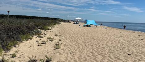 A sandy beach with a tent and a blue structure, likely a water slide, under a clear sky.