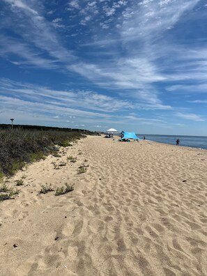 Una playa arenosa con una tienda de campaña y una estructura azul, probablemente un tobogán acuático, bajo un cielo despejado.