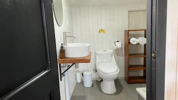 Un bagno compatto con lavandino, water e ripiano in legno con asciugamani.