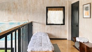 A room with a single bed, a window with curtains, a door, and a small bench with towels.