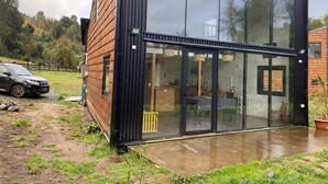 A modern building with large glass windows, a wooden exterior, and a visible interior with furniture.