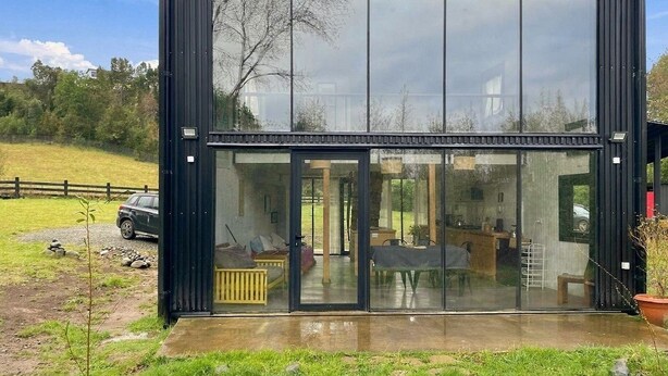 A modern, black-framed glass building with a visible interior that includes a dining area and a seating space.